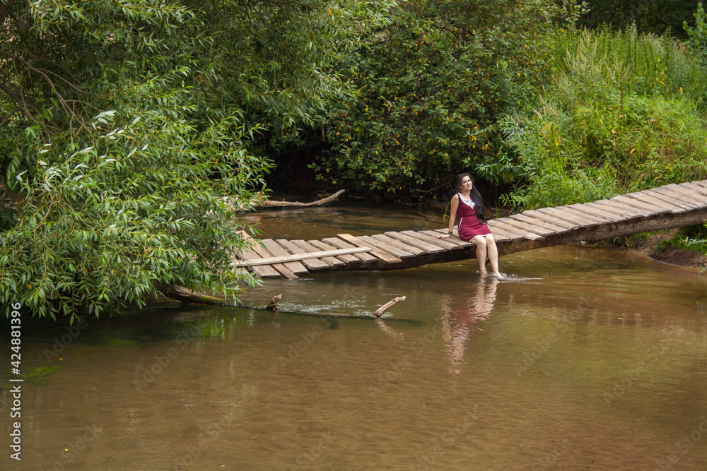 Girl sitting on a wooden bridge over the river and reading a book