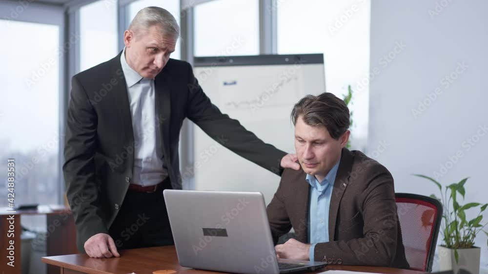 Portrait of senior Caucasian male CEO supporting young employee in office. Positive man calming down stressed colleague indoors. Business cooperation and partnership support Portrait of senior Caucasian male CEO supporting young employee in office. Positive man calming down stressed colleague indoors. Business cooperation and partnership support