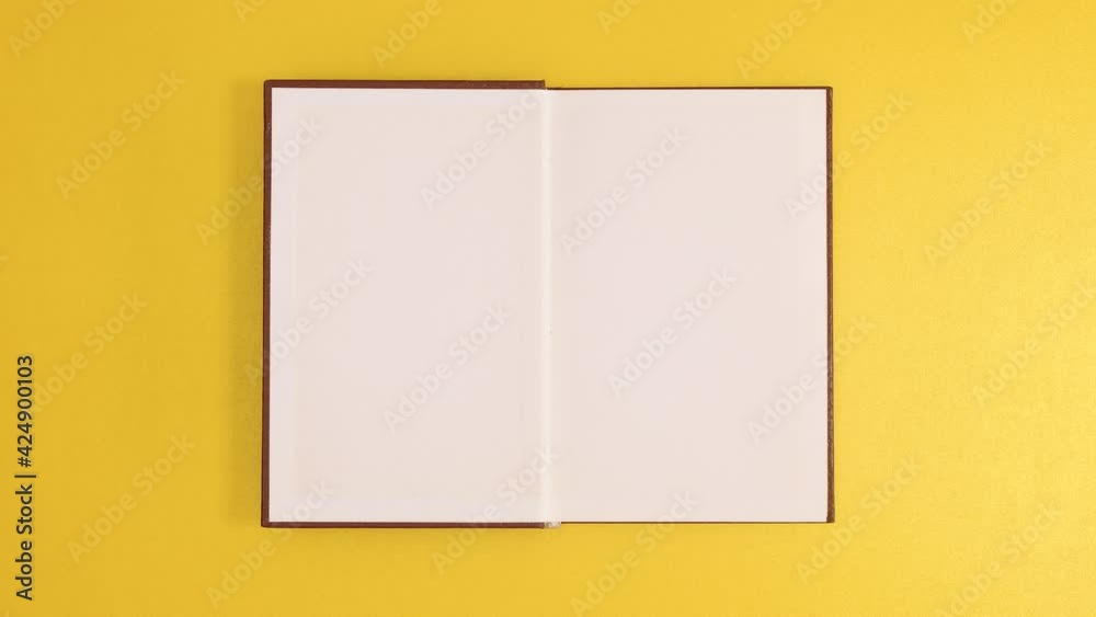 Brown vintage hardcover book appear and open with copy space on golden background. Stop motion flat lay