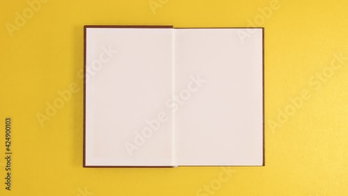 Brown vintage hardcover book appear and open with copy space on golden background. Stop motion flat lay