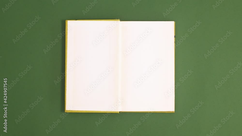 Light Green vintage hardcover book appear and open with copy space on dark green background. Stop motion flat lay