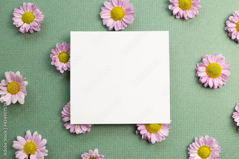 Blank memo pad with pink small flowered chrysanthemum on green background. flat lay, top view, copy space