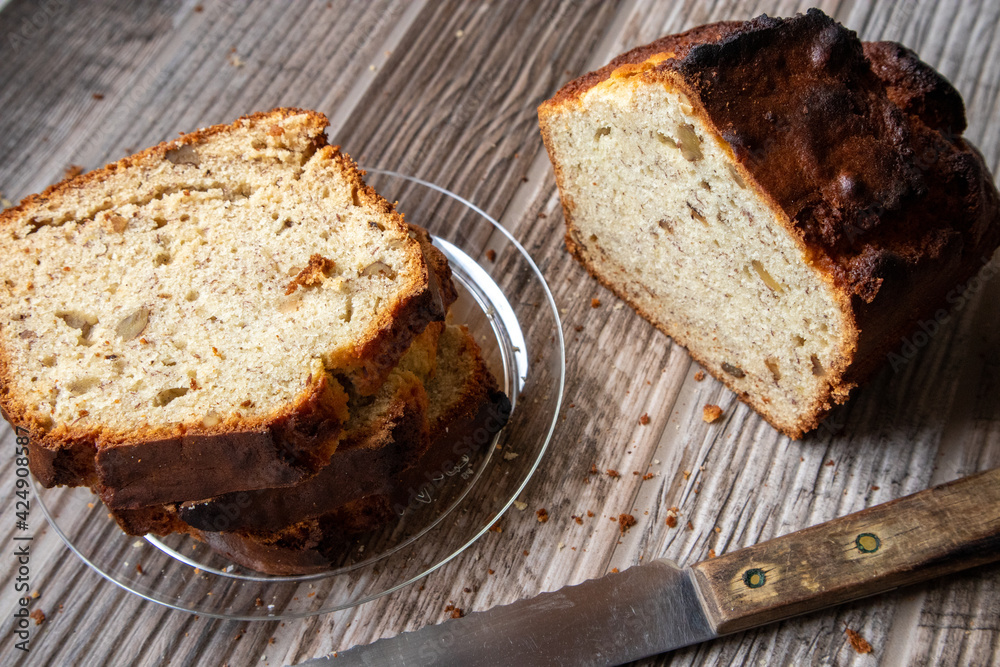 Slices of banana nut bread on a clear plate on a wood table. A loaf of bread and knife site on the table. Slices of banana nut bread on a clear plate on a wood table. A loaf of bread and knife site on the table.