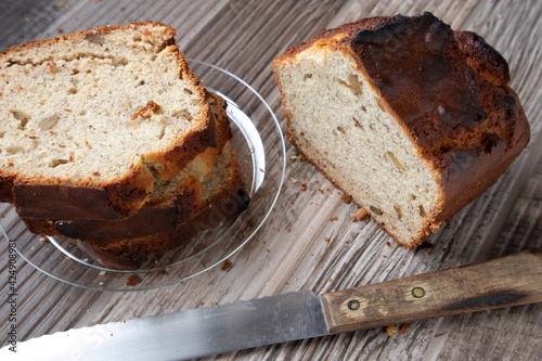 Slices of banana nut bread on a clear plate on a wood table. A loaf of bread and knife site on the table.