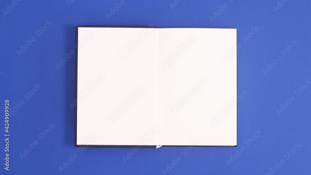 Dark Blue vintage hardcover book appear and open with copy space on blue background. Stop motion flat lay
