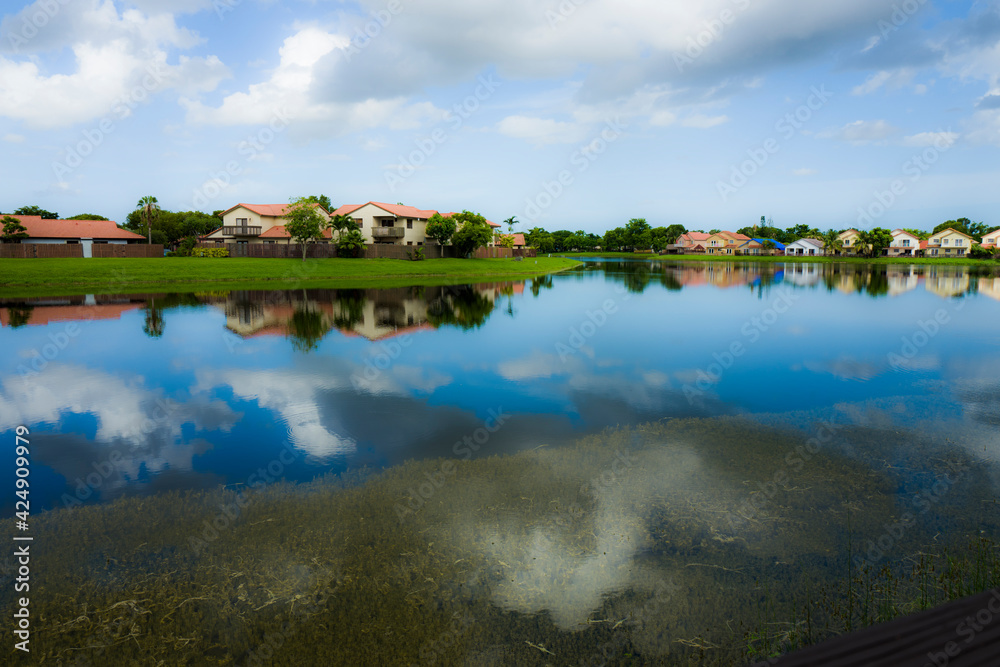 Lake waterfront houses and sky reflection at a Kendall Lakes neighborhood during a cloudy summer day in the city of Miami, Florida