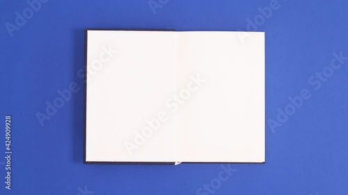 Dark Blue vintage hardcover book appear and open with copy space on blue background. Stop motion flat lay