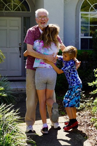 A grandfather is reunited with his granddaughter and grandson after a year apart due to the COVID pandemic. The children run to him and they hug.