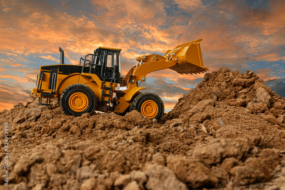 Wheel loader are digging the soil in the construction site on the sky background after sunset Wheel loader are digging the soil in the construction site on the sky background after sunset