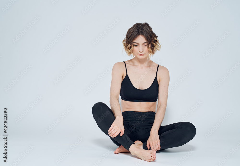 Fototapeta premium A woman is meditating with her legs crossed on the floor on a light background