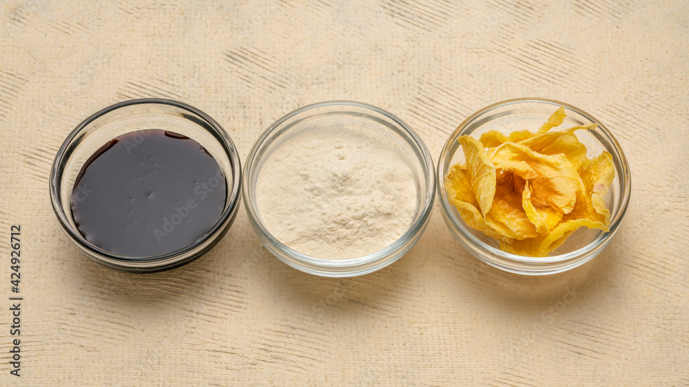 Dried slices of yacon tuber, syrup and powder in small glass bowls against textured paper. Yacon contains inulin, a complex sugar, which promotes healthy probiotics. Superfood concept.