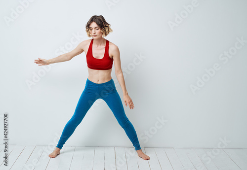 A woman in blue jeans and a red T-shirt is doing exercises with forward bends
