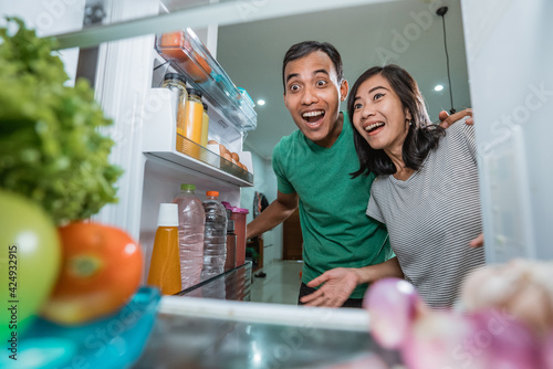 happy and excited couple open the fridge in the kitchen preparing to cook together