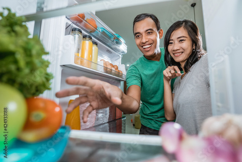 happy and excited couple open the fridge in the kitchen preparing to cook together
