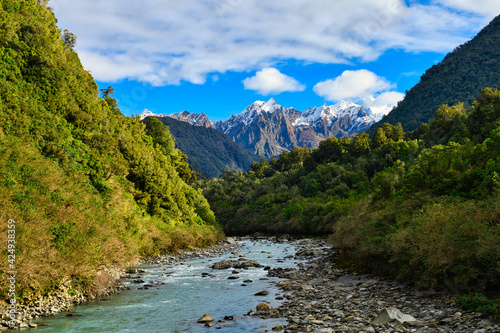 Turquoise water stream And river rocks, flowing between the mountains , In the center of the image there is a snowy mountain top, natural view in the rural of Franz Josef, South Island New Zealand
