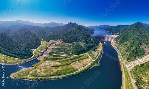 Aerial photography. Bird's eye view of the Sayano-Shushenskaya Hydroelectric Power Station. A powerful dam blocking the mountain river Yenisei, 242 meters high. Mountains and green mountain taiga