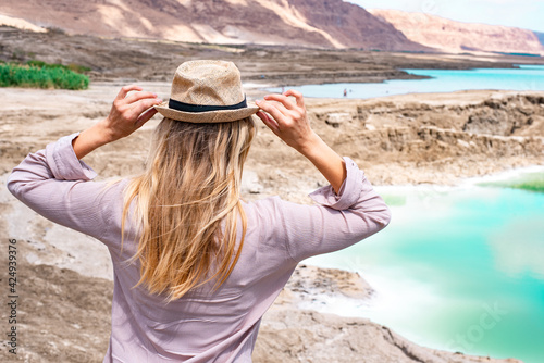 Blonde girl in hat near Dead Sea and lake full of salt. Travel and resting in summer is wonderful time to see new places and learn lot of interesting things about human life and nature. Outdoors