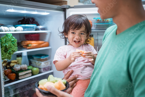 asian father and daughter open refrigerator at home having some fresh fruit together