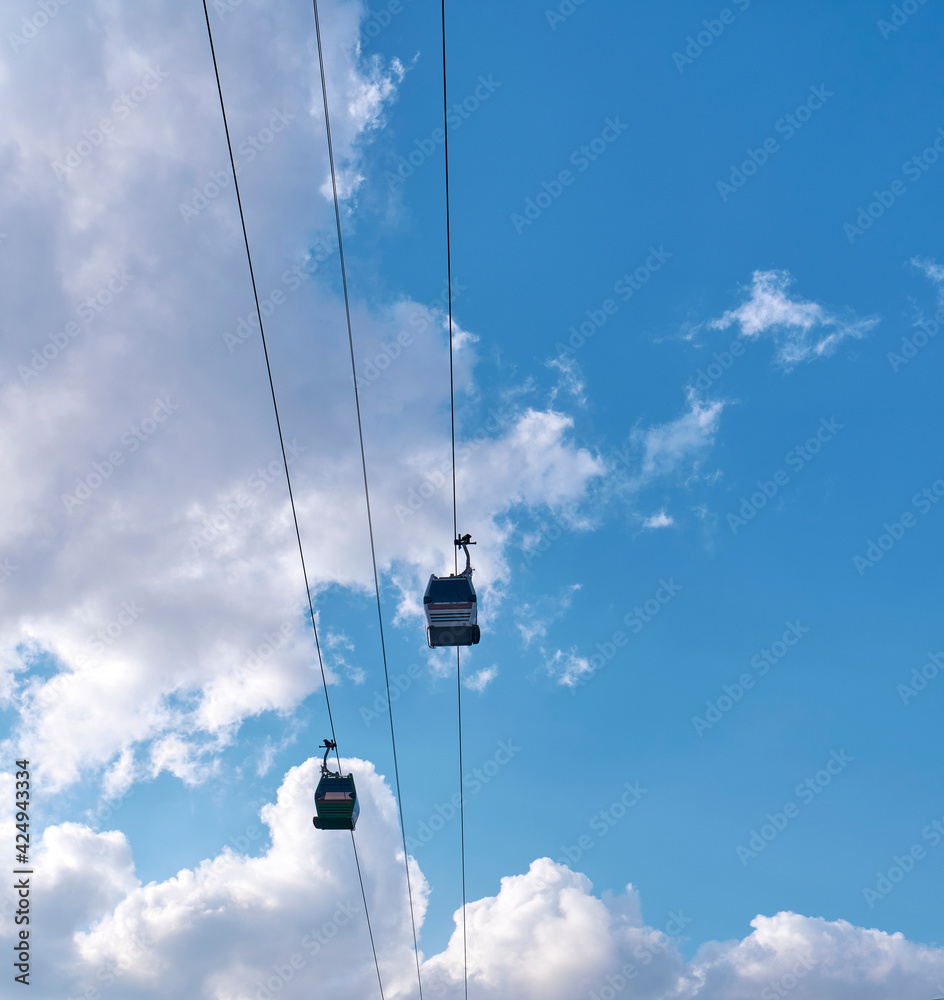 Funiculars on suspended cables move uphill against the background of a blue sky with clouds. Funiculars on suspended cables move uphill against the background of a blue sky with clouds.