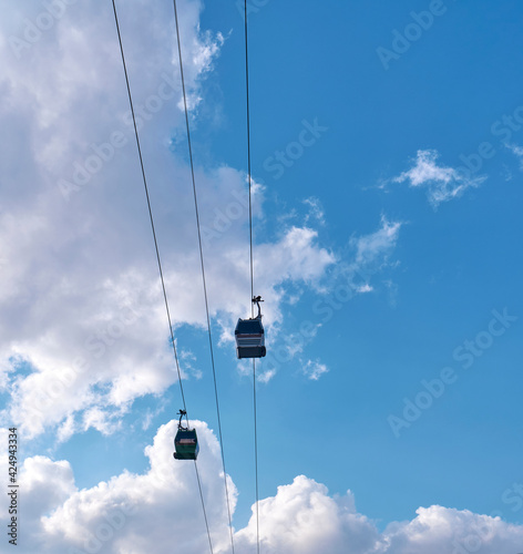 Funiculars on suspended cables move uphill against the background of a blue sky with clouds.