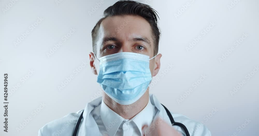 Portrait of male doctor putting on medical mask and looks at the camera over white background. Flu and Coronavirus Precautions Portrait of male doctor putting on medical mask and looks at the camera over white background. Flu and Coronavirus Precautions