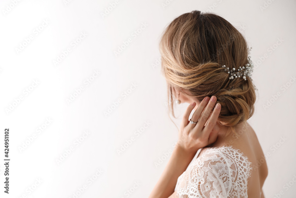 Young bride with elegant wedding hairstyle on light background, back view. Space for text Young bride with elegant wedding hairstyle on light background, back view. Space for text
