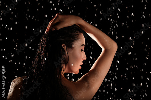Young woman washing hair while taking shower on black background