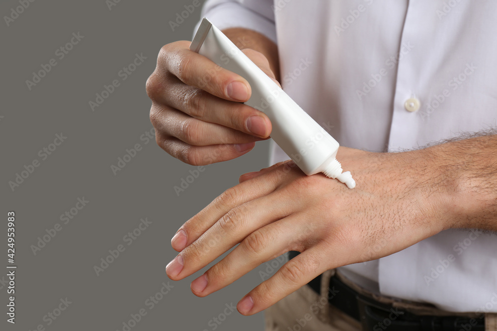Man applying cream from tube onto hand on grey background, closeup