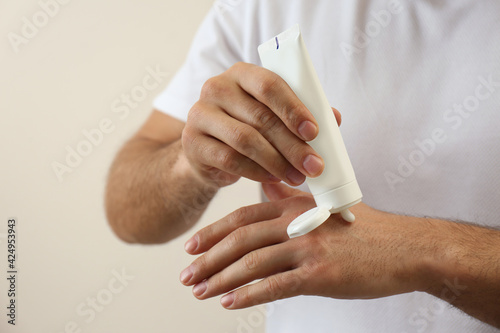 Man applying cream from tube onto hand on beige background, closeup
