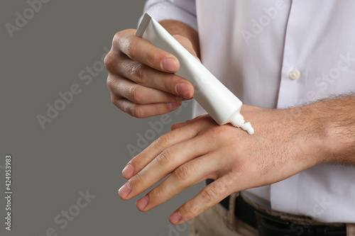 Man applying cream from tube onto hand on grey background, closeup