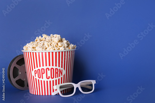 Delicious popcorn, 3D glasses and movie reel on blue background. Space for text