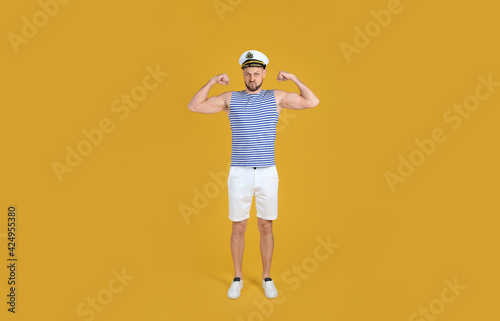 Strong sailor showing biceps on yellow background
