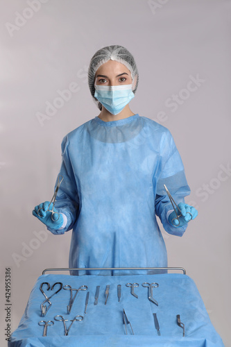 Doctor holding medical clamps near table with different surgical instruments on light background photo