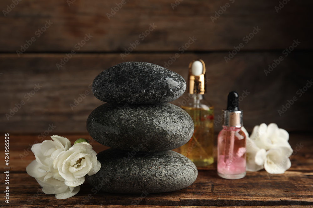 Stack of grey spa stones, flowers and oils on wooden table Stack of grey spa stones, flowers and oils on wooden table