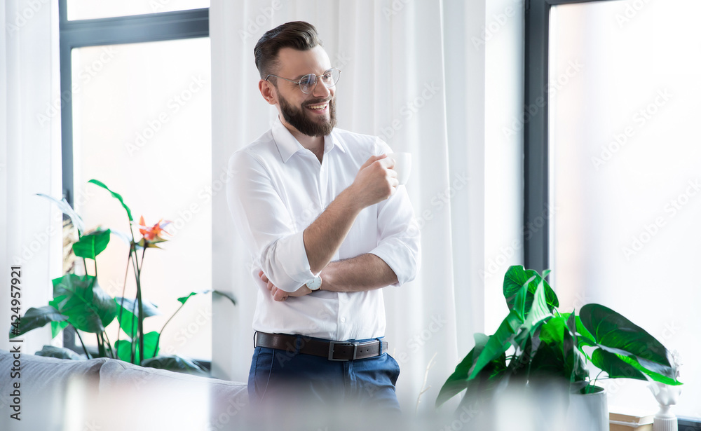 Stylish happy modern business man in smart casual wear is posing in the startup office while coffee break