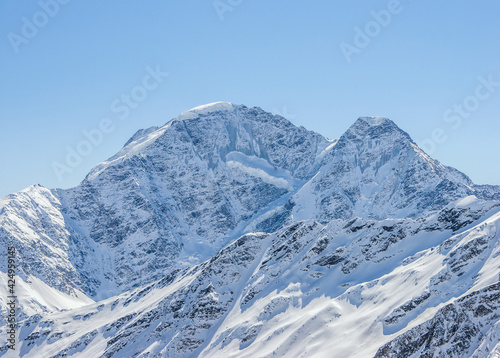 Snowy Greater Caucasus mountains Donguzorun and Nakra summits against sun shining in winter. Elbrus region, Kabardino-Balkaria, Russia.