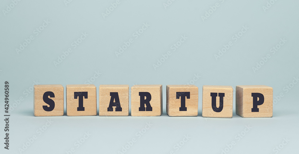 The word start up made from wooden cubes on blue background The word start up made from wooden cubes on blue background