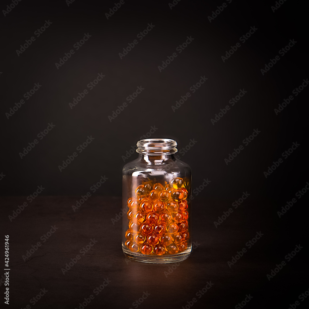 A glass jar with pills of bright orange yellow color on a brown background. A glass jar with pills of bright orange yellow color on a brown background.