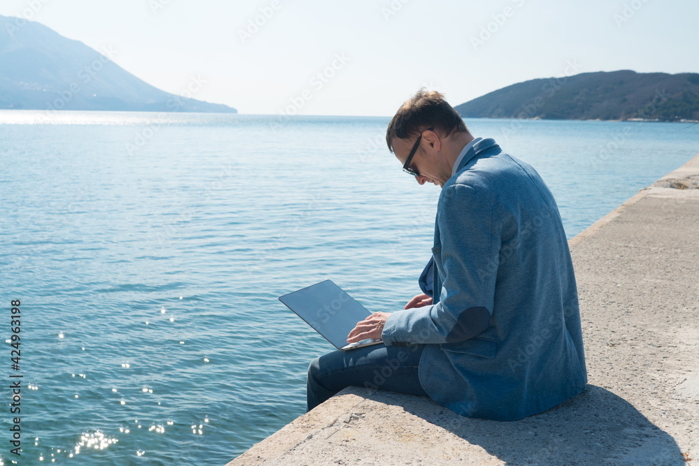 freelancer businessman working remotely on laptop while sitting on the pier