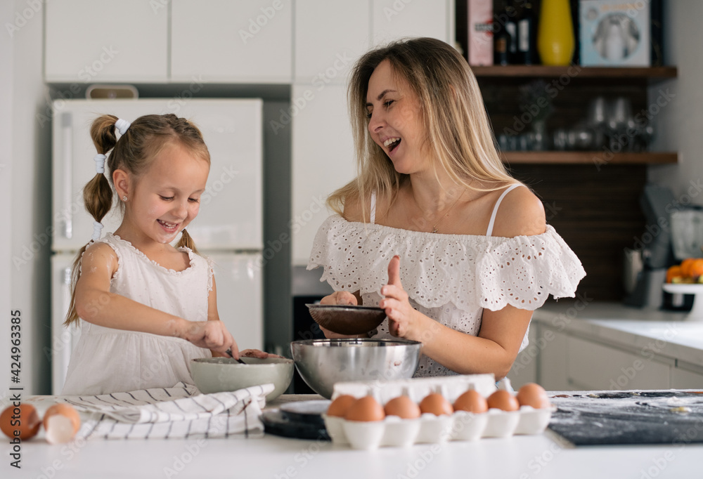 Mother and daughter with amazing smile in special clothes and funny chef cap. Cooking on kitchen cake. Kid and woman make cookie at home, make fun, enjoy. Hold mixer, on table chocolate eggs and flour Mother and daughter with amazing smile in special clothes and funny chef cap. Cooking on kitchen cake. Kid and woman make cookie at home, make fun, enjoy. Hold mixer, on table chocolate eggs and flour