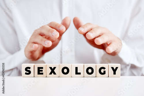 Man holds his hands over the wooden cubes with the word sexology. Sex therapist or clinical sexology photo