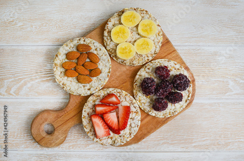 cereal breakfast crisp breads with strawberry, almonds nuts, banana fruit and blackberry on wooden cutting board top view flat lay
