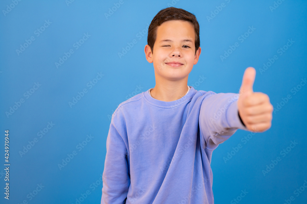 Portrait of happy boy showing thumbs up gesture, isolated over blue background Portrait of happy boy showing thumbs up gesture, isolated over blue background