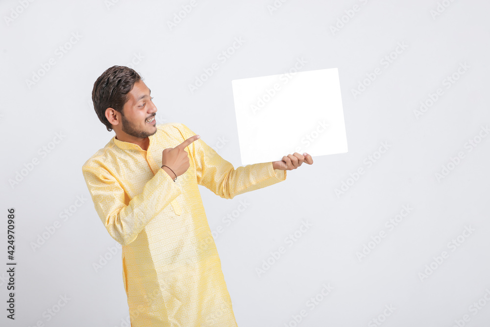 Indian man holding white board, promoting offers on festival season while wearing traditional cloths, standing over white background. Indian man holding white board, promoting offers on festival season while wearing traditional cloths, standing over white background.