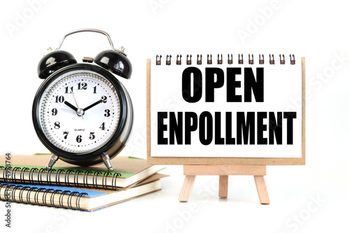 Open enrollment. text on white notepad paper on a stand next to our desk clock on a sideboard. on white background