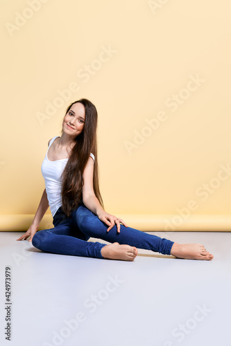 Barefoot girl in t-shirt and jeans sitting on the flook in studio