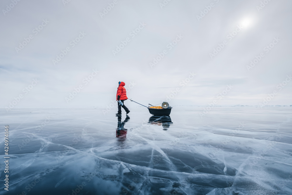 Female tourist walking with  sled dragging on the frozen ice of Lake Baikal. Winter trekking
