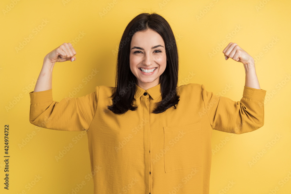 Portrait of cheerful young girl bending biceps isolated on orange background. Smiling girl on the background of an empty wall.
