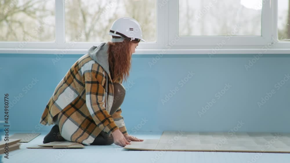 woman builder in helmet lays laminate on floor insulated with polyester foam in apartment during renovation woman builder in helmet lays laminate on floor insulated with polyester foam in apartment during renovation