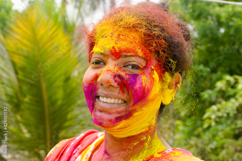 Fototapeta Naklejka Na Ścianę i Meble -  Portrait Of One Young Indian Happy woman with pink, yellow and red Holi colored powder paint on face During Holi Color festival. Front View. Looking at camera.